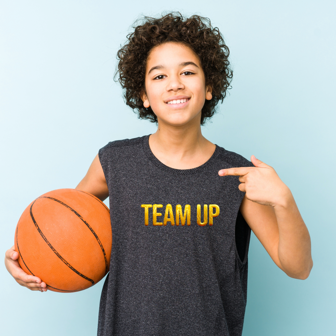 Young player holding a basketball, pointing to his Team Up jersey
